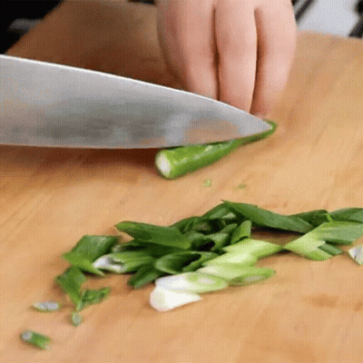A Person Is Cutting Green Onions With A Knife On A Cutting Board GIF