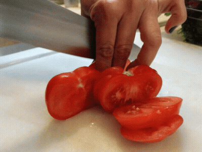 A Person Is Cutting Tomatoes On A White Cutting Board GIF
