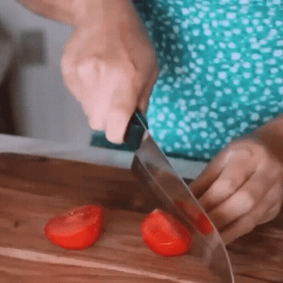 A Person Is Cutting Two Tomatoes On A Wooden Cutting Board . GIF