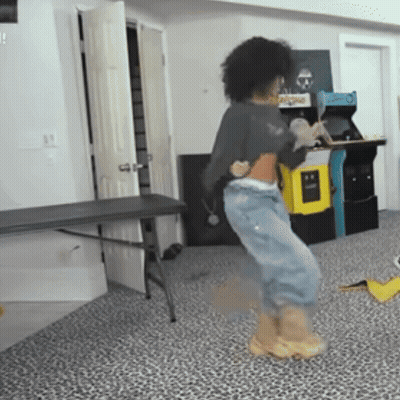 A Person Is Dancing In A Room With An Arcade Machine In The Background And A Table In The Foreground GIF