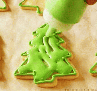 A Person Is Decorating A Cookie In The Shape Of A Christmas Tree GIF