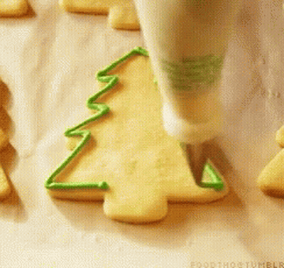 A Person Is Decorating A Cookie In The Shape Of A Christmas Tree With Green Frosting GIF