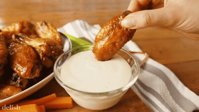 A Person Is Dipping A Chicken Wing Into A Bowl Of Ranch Dressing GIF