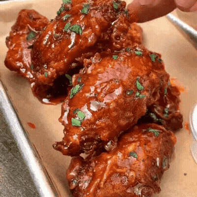 A Person Is Dipping A Chicken Wing Into A Sauce On A Tray . GIF