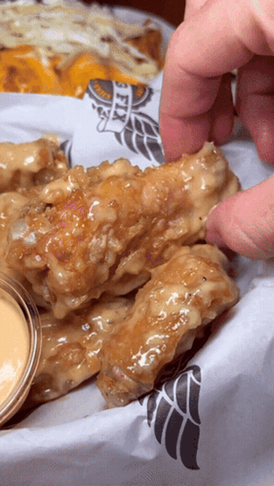 A Person Is Dipping A Chicken Wing Into A Sauce That Says Wings GIF