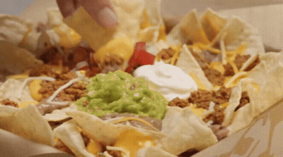 A Person Is Dipping A Chip Into A Bowl Of Nachos With Guacamole And Sour Cream GIF