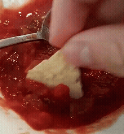 A Person Is Dipping A Cracker In A Bowl Of Tomato Sauce . GIF