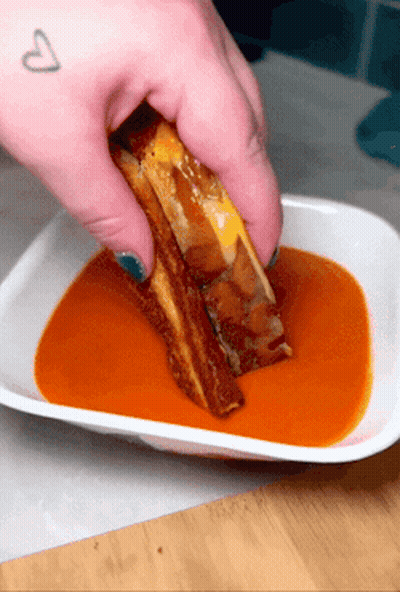 A Person Is Dipping A Grilled Cheese Sandwich In A Bowl Of Sauce GIF