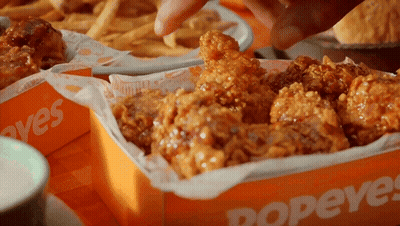 A Person Is Dipping A Piece Of Fried Chicken Into A Box That Says Popeyes GIF