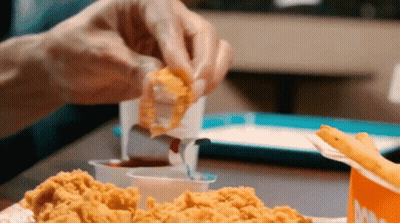 A Person Is Dipping A Piece Of Fried Chicken Into A Sauce GIF