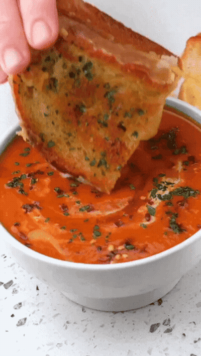 A Person Is Dipping A Piece Of Grilled Cheese Into A Bowl Of Soup GIF