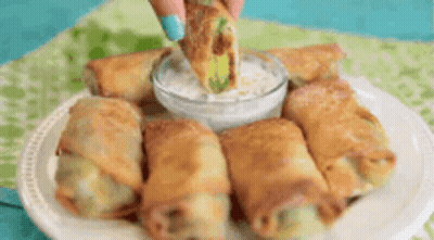 A Person Is Dipping An Egg Roll In Ranch Dressing On A Plate Of Food . GIF