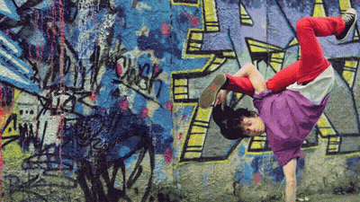 A Person Is Doing A Handstand In Front Of A Wall With Graffiti On It Including The Letter R GIF