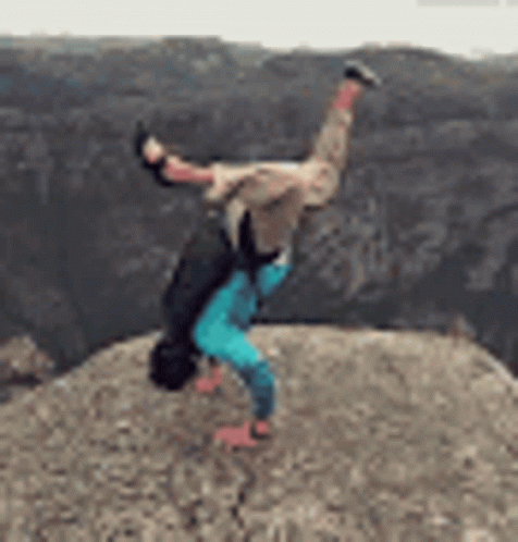 A Person Is Doing A Handstand On The Edge Of A Cliff . GIF