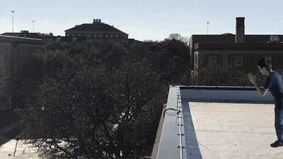 A Person Is Doing A Trick On A Rooftop With A Building In The Background GIF