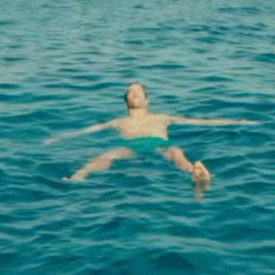 A Person Is Floating On Their Stomach In The Ocean . GIF