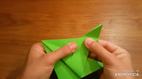 A Person Is Folding A Green Origami Piece On A Wooden Table GIF