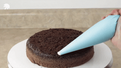 A Person Is Frosting A Chocolate Cake With A Blue Bag That Says Youtube On The Bottom GIF