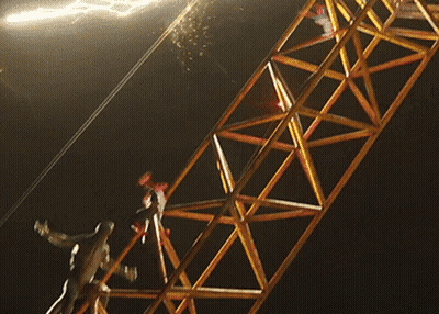 A Person Is Hanging From A Metal Structure With A Light Behind Them GIF