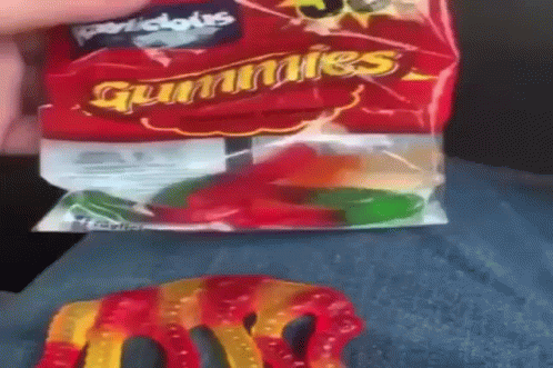 A Person Is Holding A Bag Of Gummy Worms On Their Lap . GIF