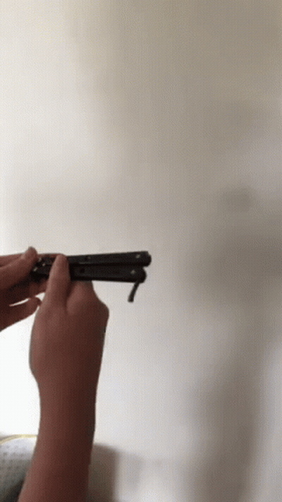 A Person Is Holding A Black Butterfly Knife In Front Of A White Wall GIF