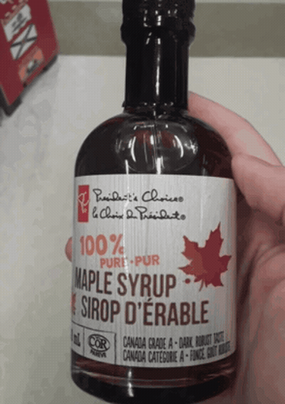 A Person Is Holding A Bottle Of Maple Syrup In Their Hand GIF