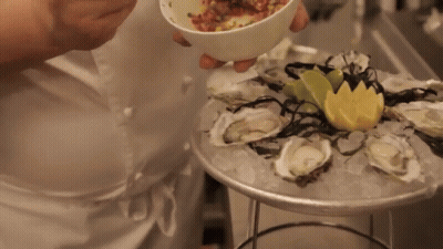 A Person Is Holding A Bowl Of Food Over A Plate Of Oysters And Ice GIF