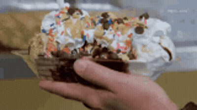 A Person Is Holding A Bowl Of Ice Cream With Sprinkles On It . GIF