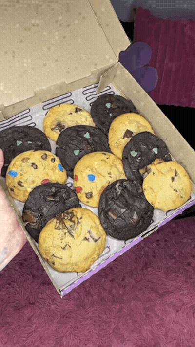 A Person Is Holding A Box Of Cookies With Different Flavors On Them GIF