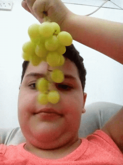 A Person Is Holding A Bunch Of Grapes To Their Face GIF