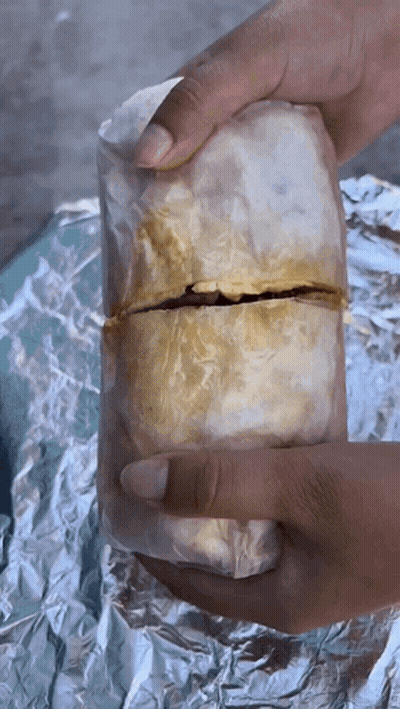 A Person Is Holding A Burrito Wrapped In Foil GIF