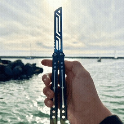 A Person Is Holding A Butterfly Knife In Front Of The Water GIF