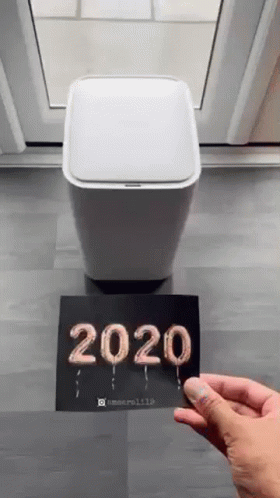 A Person Is Holding A Card That Says `` 2020 '' Next To A Trash Can . GIF