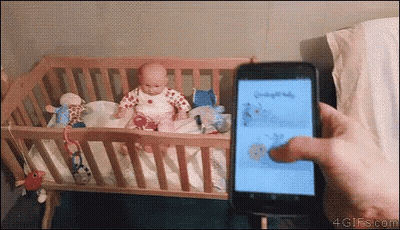 A Person Is Holding A Cell Phone In Front Of A Crib With A Baby In It .. GIF