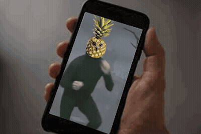 A Person Is Holding A Cell Phone With A Pineapple On Their Face GIF