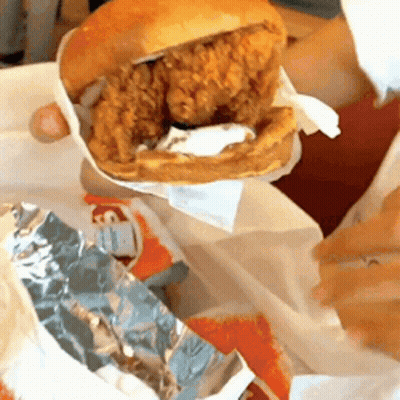 A Person Is Holding A Chicken Sandwich On A Bun GIF