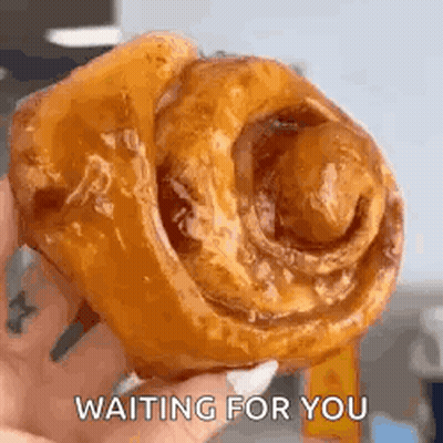 A Person Is Holding A Cinnamon Roll In Their Hand And Waiting For You . GIF