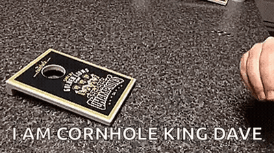 A Person Is Holding A Cornhole Board On A Table . GIF