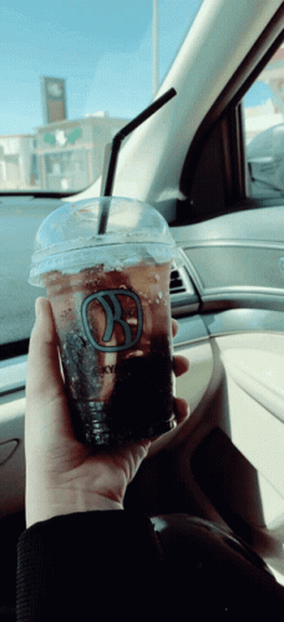 A Person Is Holding A Cup Of Coffee With A Straw In A Car GIF