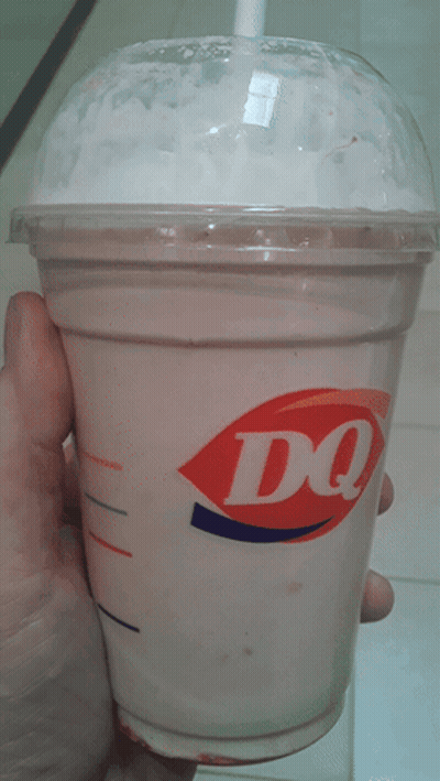 A Person Is Holding A Cup Of Dq Milkshake In Their Hand GIF