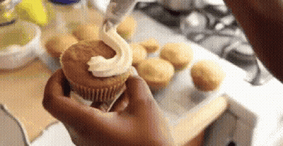 A Person Is Holding A Cupcake With Frosting On It In Their Hand . GIF