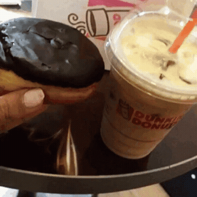 A Person Is Holding A Donut Next To A Dunkin Donuts Cup Of Coffee GIF