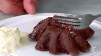 a person is holding a fork over a piece of red velvet cake on a plate with ice cream .