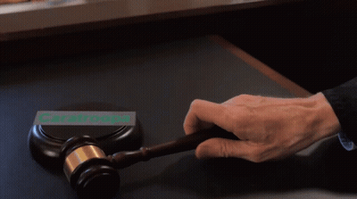 A Person Is Holding A Gavel In Front Of A Sign That Says Caratroops GIF