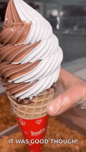 A Person Is Holding A Giant Ice Cream Cone With Chocolate And White Icing . GIF
