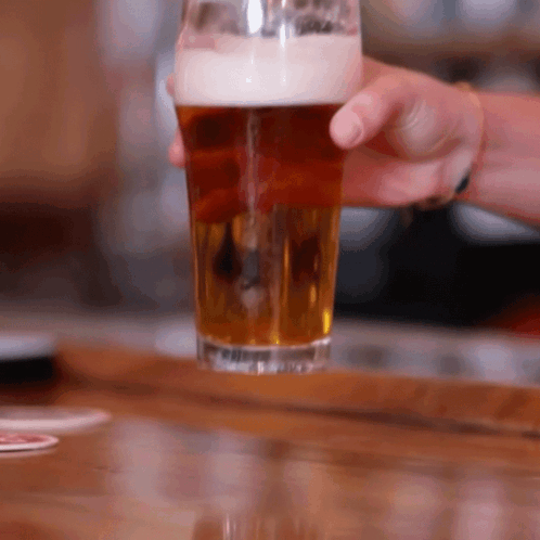 A Person Is Holding A Glass Of Beer On A Bar GIF