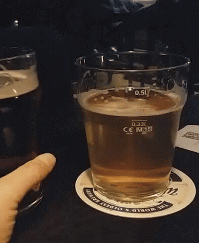 A Person Is Holding A Glass Of Beer On A Coaster That Says The World 'S Oldest Brewing GIF