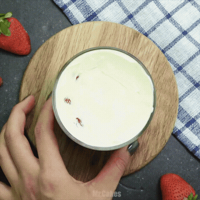 A Person Is Holding A Glass Of Milk On A Wooden Cutting Board With The Words Mr. Cakes Written On The Bottom GIF