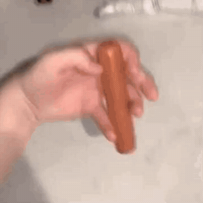 A Person Is Holding A Hot Dog In Their Hand On A Counter . GIF