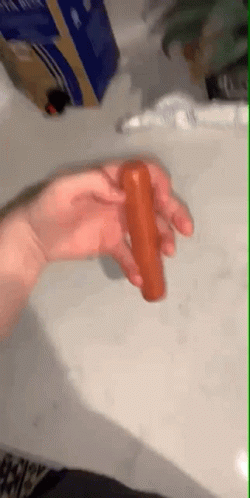 A Person Is Holding A Hot Dog In Their Hand On A Table . GIF